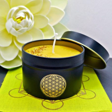 Schwarze Kerze in einer Dose mit goldener Verzierung, umgeben von einer weißen Blüte.